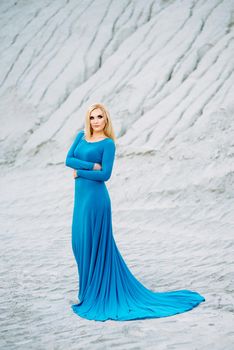 blonde girl in a blue dress with blue eyes in a granite quarry against the background of gravel