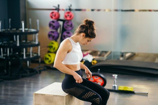 Athletic woman doing squats on box as part of exercise routine. Caucasian female doing box jump workout at gym.