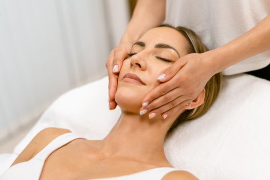 Middle-aged woman having a head massage in a beauty salon. Body care treatment in a beauty centre.