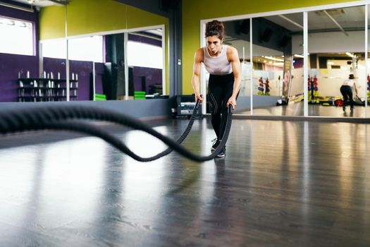 Young and athletic woman using training ropes in a gym. Fitness concept.