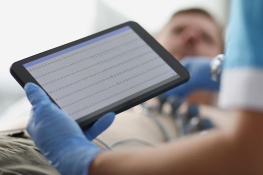 Close-up of nurse holding monitor with cardiogram, screen displaying vital signs like heart rate. Medical worker take care of patients. Medicine, healthcare, hospital concept. Blurred background
