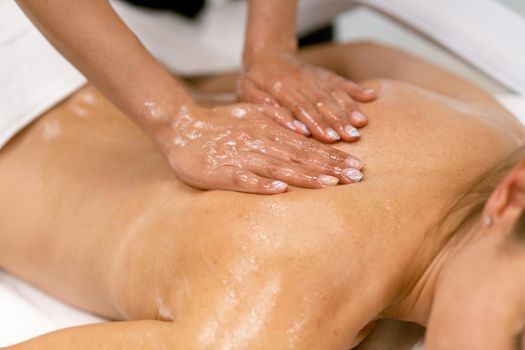 Woman receiving a back massage with massage candle oil. Body care treatment in a beauty centre.