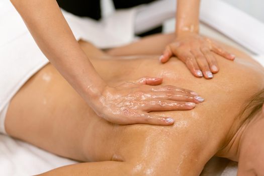 Woman receiving a back massage with massage candle oil. Body care treatment in a beauty centre.