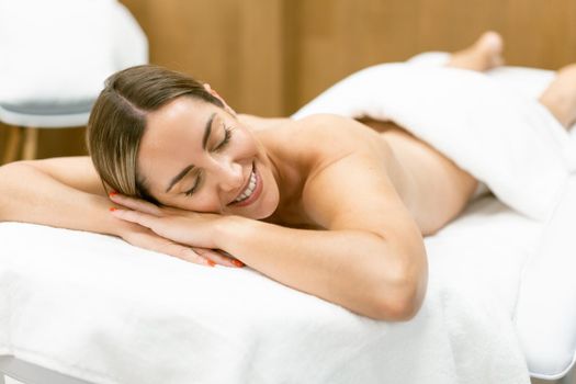 Middle-aged woman lying on a beauty parlour couch for a relaxing massage. Smiling female.