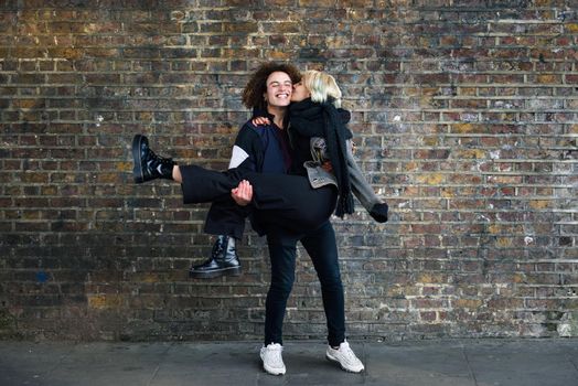 Man holding his girlfriend in his arms. Young couple enjoying Camden town in front of a brick wall typical of London, UK