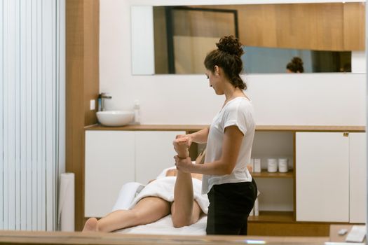 Middle-aged woman having a leg massage in a beauty salon. Body care treatment in a beauty centre.