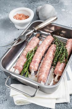 Raw Bratwurst pork meat sausages in a kitchen tray. Gray background. Top view.
