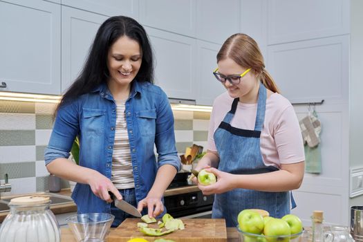 Family, relationships, lifestyle. Mom and teen daughter cooking apple pie together at home kitchen