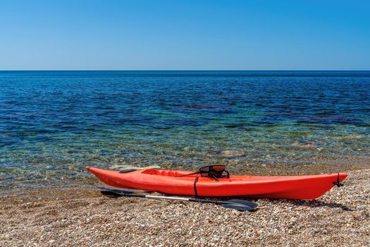 Red kayak on an isolated rocky beach, against the background of a the sea. The concept of an active life in harmony with nature