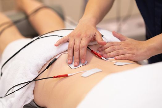 Physiotherapist applying electro stimulation in physical therapy to a young woman.