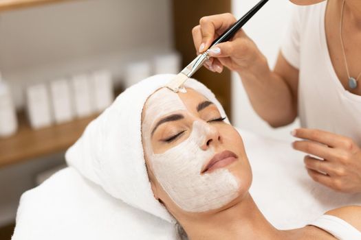 Aesthetics applying a mask to the face of a Middle-aged woman in modern wellness center. Beauty and Aesthetic concepts.