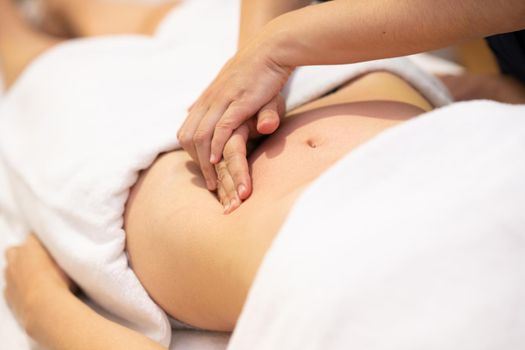 Woman receiving a belly massage at spa salon. Female patient is receiving treatment by professional osteopathy therapist.