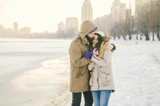 Theme love and date on nature. A young Caucasian heterosexual couple guy and girl walk in the winter along a frozen lake in winter. Bearded Man Hugging Woman. Valentine's day holiday.