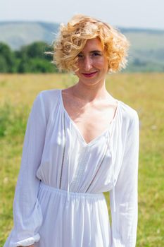 Beautiful blonde woman with short curly hair outdoors. Romantic model in summer white dress.