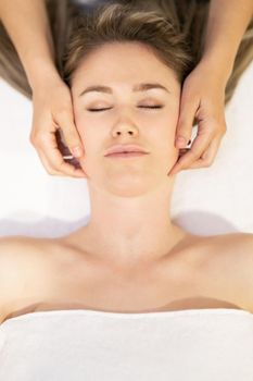 Young woman receiving a head massage in a spa center. Female patient is receiving treatment by professional therapist.