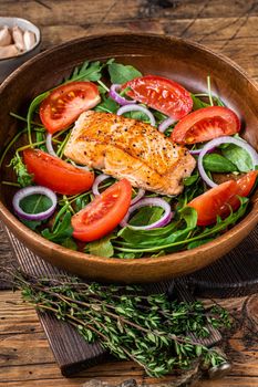 Salmon steak salad with green leaves arugula, avocado and tomato in a wooden plate. Wooden background. Top view.