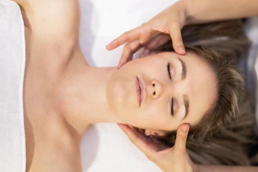 Young woman receiving a head massage in a spa center. Female patient is receiving treatment by professional therapist.