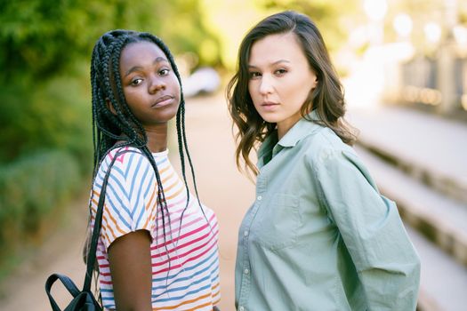 Two young friends looking at camera together on the street. Multiethnic women.