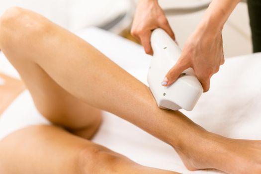 Beautiful woman receiving legs laser hair removal at a beauty center.