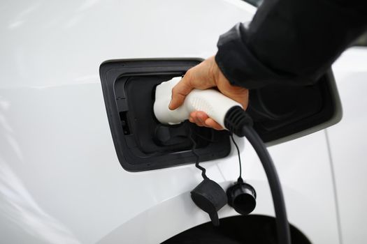 Close-up of hand holding fuel nozzle to add gas at petrol station, refueling car with diesel. Clean white automobile on parking. Vehicle, maintenance, transportation, ownership concept