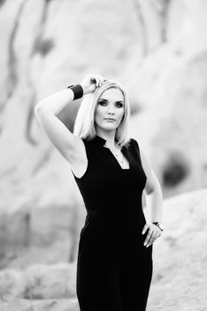 blonde girl in a black trouser suit with blue eyes on the background of a granite quarry from gray rubble