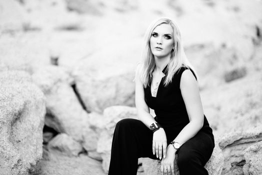 blonde girl in a black trouser suit with blue eyes on the background of a granite quarry from gray rubble