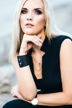 blonde girl in a black trouser suit with blue eyes on the background of a granite quarry from gray rubble