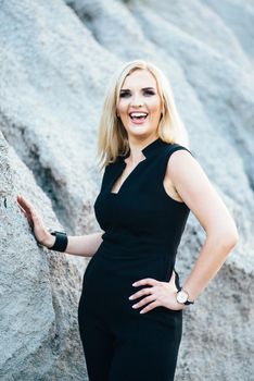 blonde girl in a black trouser suit with blue eyes on the background of a granite quarry from gray rubble