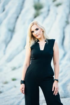 blonde girl in a black trouser suit with blue eyes on the background of a granite quarry from gray rubble