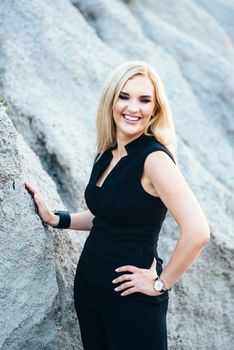 blonde girl in a black trouser suit with blue eyes on the background of a granite quarry from gray rubble