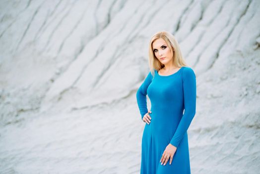 blonde girl in a blue dress with blue eyes in a granite quarry against the background of gravel