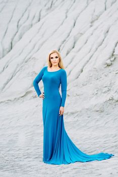 blonde girl in a blue dress with blue eyes in a granite quarry against the background of gravel