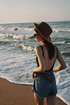 cheerful woman in sunglasses and a hat walks along the ocean. High quality photo