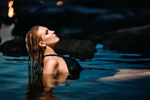 blonde girl in a black dress with blue eyes on the stone coast of the river