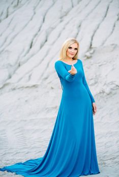 blonde girl in a blue dress with blue eyes in a granite quarry against the background of gravel