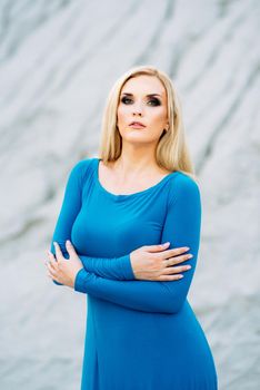 blonde girl in a blue dress with blue eyes in a granite quarry against the background of gravel