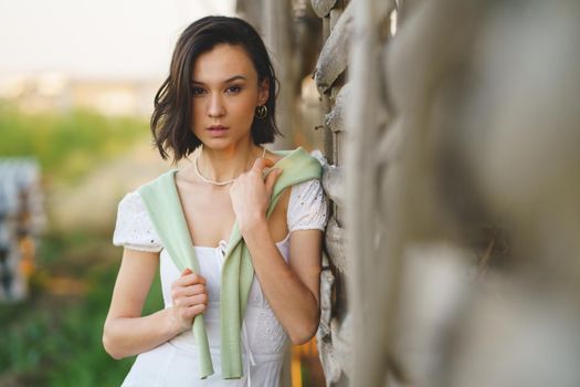 Pretty young Asian woman, posing near a tobacco drying shed, wearing a white dress and green wellies. Beauty and fashion concept