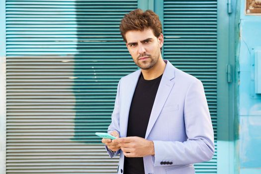 Young businessman wearing blue suit using a smartphone in urban background. Man with formal clothes in the street.