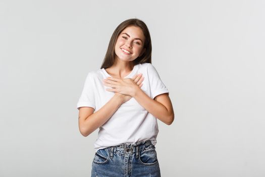 Touched happy young woman smiling, holding hands on chest, feeling thankful.