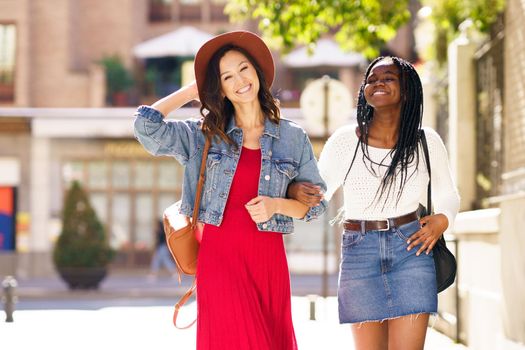 Two friends walking together on the street. Multiethnic women.