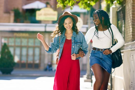 Two friends walking together on the street. Multiethnic women.