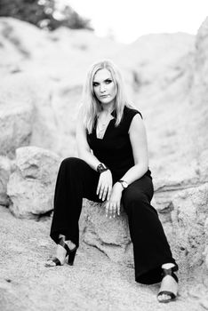 blonde girl in a black trouser suit with blue eyes on the background of a granite quarry from gray rubble