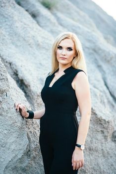 blonde girl in a black trouser suit with blue eyes on the background of a granite quarry from gray rubble