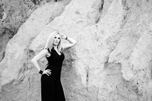 blonde girl in a black trouser suit with blue eyes on the background of a granite quarry from gray rubble