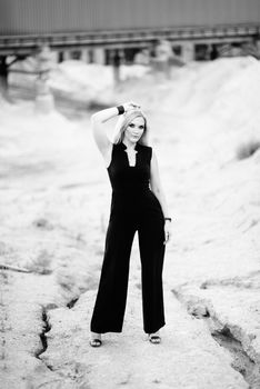 blonde girl in a black trouser suit with blue eyes on the background of a granite quarry from gray rubble