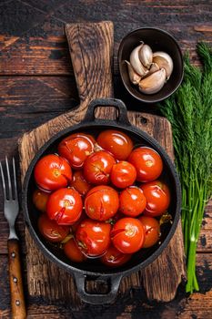 Salted Pickled cherry tomatoes in a pan with herbs and dill. Dark wooden background. Top view.