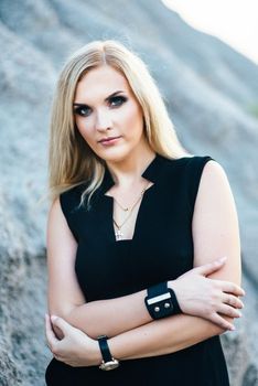 blonde girl in a black trouser suit with blue eyes on the background of a granite quarry from gray rubble