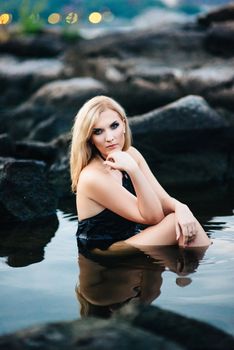 blonde girl in a black dress with blue eyes on the stone coast of the river