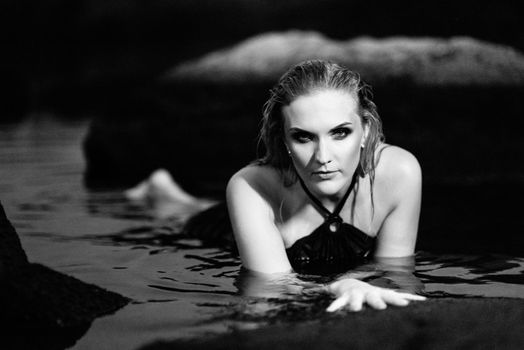 blonde girl in a black dress with blue eyes on the stone coast of the river