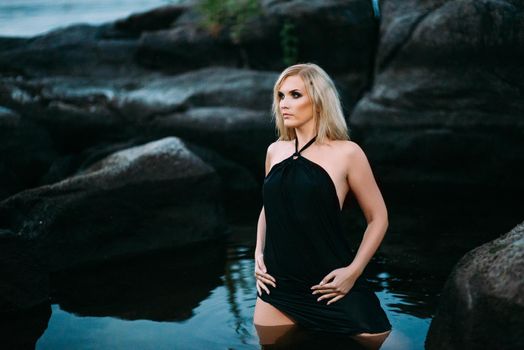 blonde girl in a black dress with blue eyes on the stone coast of the river